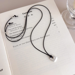 Detail of brushed silver square pendant on black cord over a vintage book page