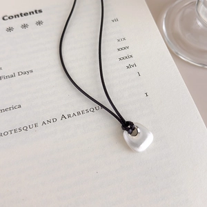 Macro detail of a brushed pebble-shaped pendant on a black cord over an open book