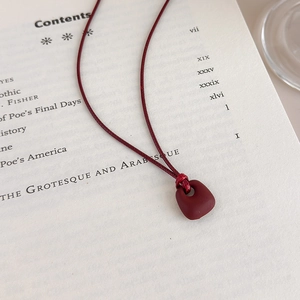 Detailed close-up of dark red matte square pendant on woven rope necklace over a book