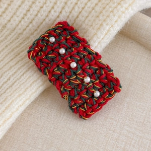 Close-up of hand-knitted Christmas hair clip with red green yarn and white pearls