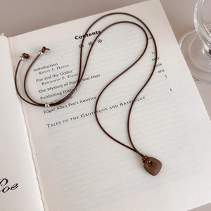 Close-up of matte brown pendant on wax rope over a vintage book with silver beads