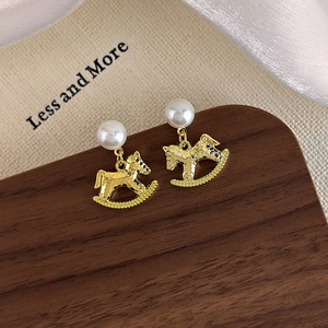 Close-up of pearl stud earrings with golden hammered rocking horse pendants on silk