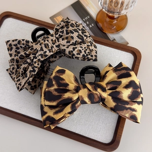 Detail view of two leopard print bow claw clips with brown fabric and black plastic teeth