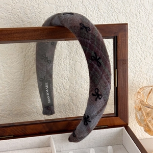 Detail of grey wool headband with black bow patterns and handmade label on wood