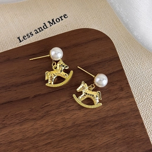 Detail of golden rocking horse earrings with pearls on wood and fabric display