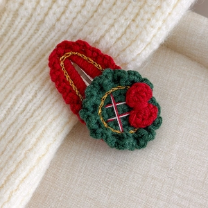 Close-up of handmade knitted Christmas hair clip with red and green festive wreath pattern