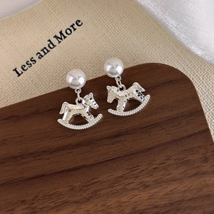 Detail of silver rocking horse earring with pearl on elegant walnut wood surface