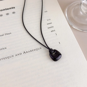 Minimalist black rectangle pendant necklace displayed on an open vintage book page