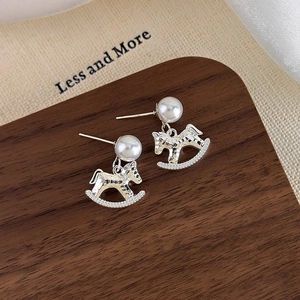 Close-up of silver rocking horse earrings with pearls on dark walnut wood
