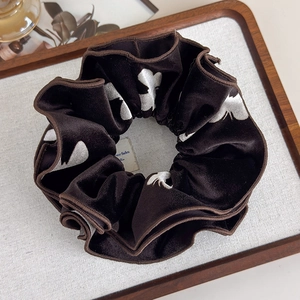 Detailed texture of brown velvet scrunchie with white butterfly print on wooden tray