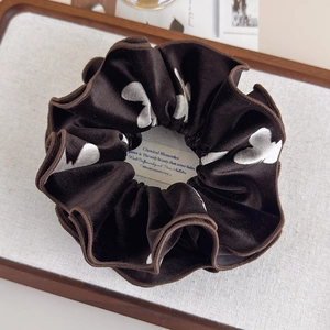 Detailed close-up of dark brown velvet scrunchie with silver heart patterns on a tray