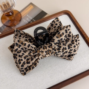 Detail shot of leopard print fabric bow hair claw clip on a rustic wooden tray