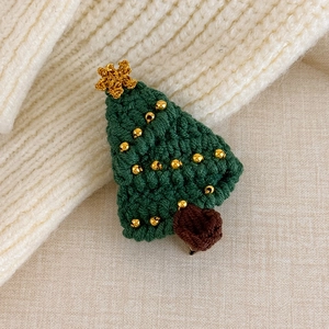Detailed view of a hand-knitted green Christmas tree hair clip on a cozy white sweater
