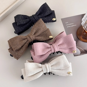 Close-up of four wool fabric bow hair clips in grey, brown, pink, and beige colors