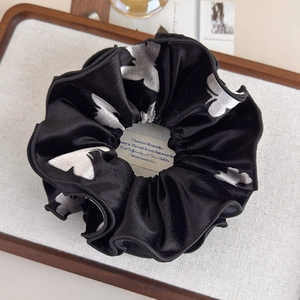 Detail of a large black velvet scrunchie with silver butterfly prints on a wooden tray