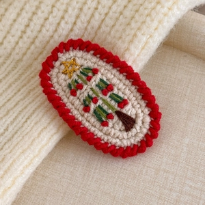 Close-up of handmade knit Christmas tree hair clip with red scalloped edges and gold star