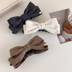 Close-up of textured fabric bow hair claws in grey, beige and brown with gold metallic details