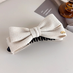 Detail of cream wool bow hair clip showing ribbed fabric texture and gold metal accent