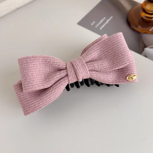 Close-up of pink knit bow hair clip with golden love tag and textured wool fabric