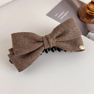 Detail of a brown ribbed knit double-layered bow hair claw with gold oval accent