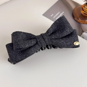 Detail of wool fabric bow hair claw clip in dark grey with a small gold emblem