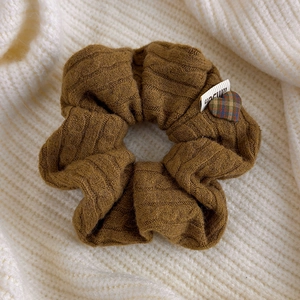 Detail of cable knit caramel brown scrunchie with a plaid heart charm and woven label