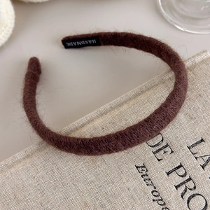Detail of dark brown plush headband with handmade label on beige linen texture background