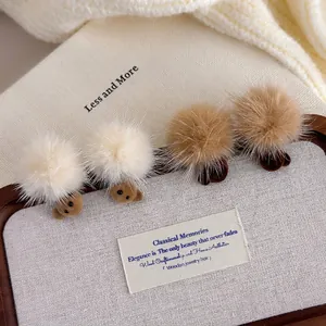 Winter faux fur pom-pom bear earrings in cream and brown on a minimalist linen display