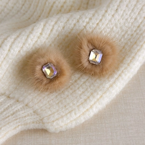 Close-up of fluffy light brown pom-pom earrings with a sparkling rectangular crystal center