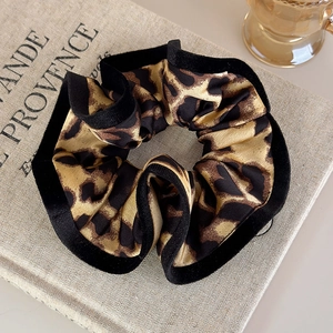 Detail of leopard print scrunchie with black velvet piping on a textured book