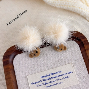 Detail of plush brown bear hair clips with cream pom-poms on a cozy autumn fabric background