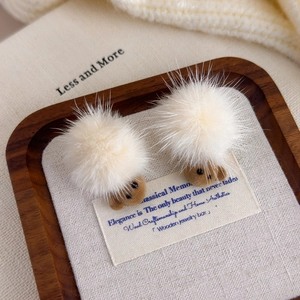 Detailed close-up of teddy bear earrings with white pom-pom and brown flocked texture