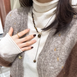 Detail of tiger eye stone necklace and gold ring styled on a white turtleneck sweater