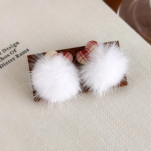 Détail de boucles d'oreilles boules de poils blanches avec des accents à carreaux