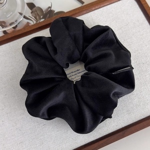 Détail d'un chouchou en tissu sergé noir avec étiquette tissée sur un plateau en bois