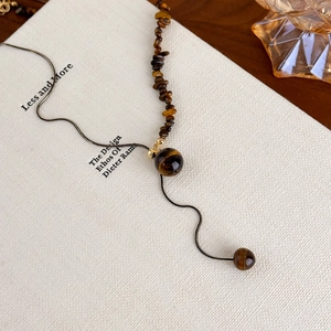 Detailed view of irregular tiger eye stone necklace draped over an aesthetic book cover