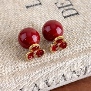 Detail view of red zircon flower earrings with large red beads on textured linen fabric