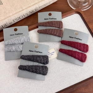 Detailed set of knitted triangle hair clips in grey, red, and brown on a wooden tray