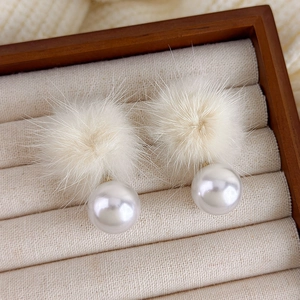Detailansicht der flauschigen Pelzball- und Perlenohrringe auf beige Samt-Schmucktablett