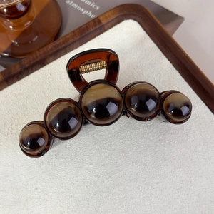 Détail de la grande pince à cheveux en acrylique marron au design sphérique sur bois