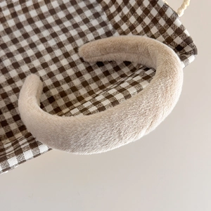 Gros plan du serre-tête beige en fausse fourrure sur un plateau en tissu à carreaux