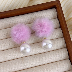 Detailansicht lila flauschiger Pompons und großer weißer Perlenohrringe auf einem Holztablett