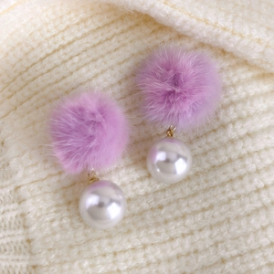 Detail von lavendelfarbenem Plüschball und Perlenohrringen auf Strickhintergrund