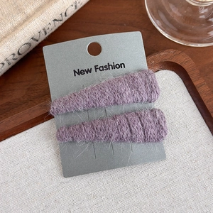 Close-up of two purple plush triangle hair clips set on a display card for styling