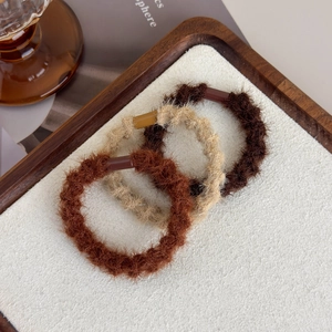 Detail view of plush velvet hair ties in earthy tones on a rustic wooden tray