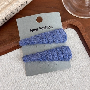 Detail of two blue knitted triangle hair clips on a New Fashion card over a wooden tray