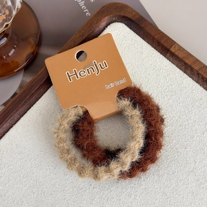Close-up of two plush elastic hair bands in brown and beige on a wooden tray