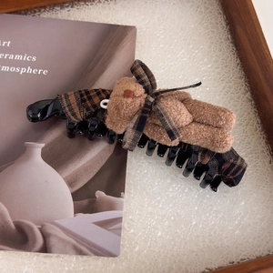 Détail d'une pince à cheveux ours en peluche avec nœud à carreaux marron