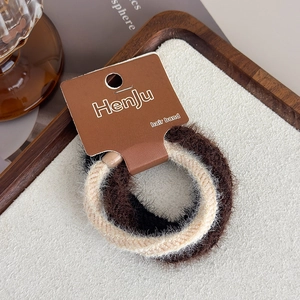 Detail view of plush hair scrunchies in beige and brown on a wooden display tray