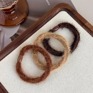 Close-up of three plush elastic hair ties in brown and beige on a wooden tray